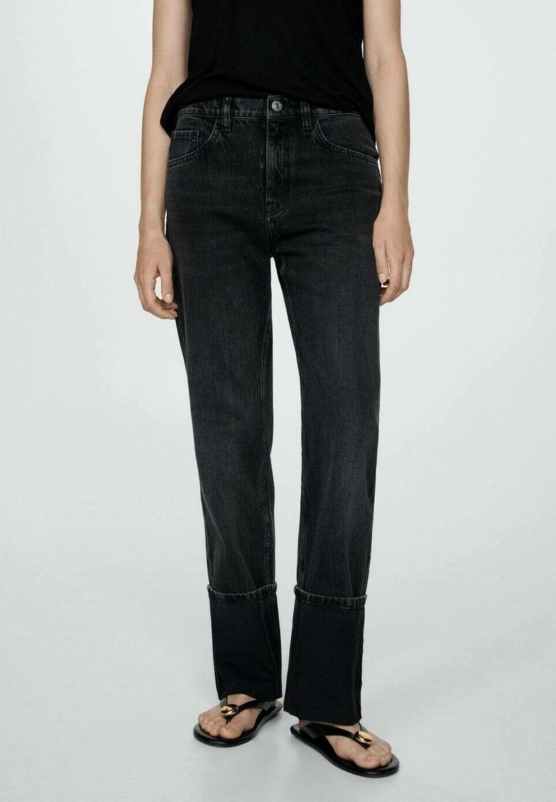 Jeans de mezclilla negros con corte recto, presentando un dobladillo deshilachado y detalles de costura sutiles. Combinados con sandalias negras.