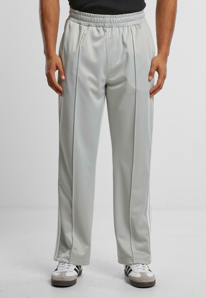 Lys grå joggebukser laget av glatt stoff med en elastisk midje, med hvite side-striper og frontfold.