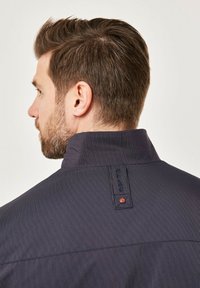 Navy striped jacket with a high collar, featuring a small red accent at the back and a smooth, textured fabric.