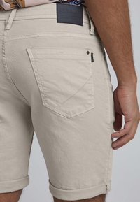 Beige shorts laget av bomullsmiks, med rullet kant, baklommer med chevrondesign og et lærmerkelapp på livet.
