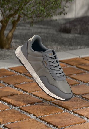Gray sneaker with a smooth texture, featuring a white sole and light gray accents. Displays a lace-up design with branding detail.