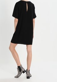 Robe noire à manches courtes avec une ouverture en forme de clé dans le dos, associée à des bottines imprimé léopard noir et blanc avec un gros talon.
