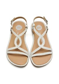 Sandali in pelle intrecciata bianca con suola piatta, caratterizzati da un design incrociato e una tomaia alla caviglia, su uno sfondo di una soletta marrone.