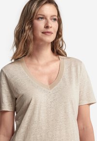 Beige v-hals t-shirt med korte ærmer, der har en tekstureret finish og ribbet halsudskæring. Let og blødt stofsammensætning.