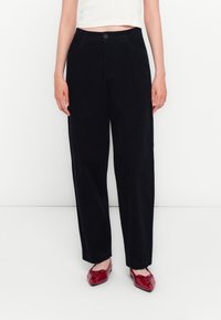 Donkerblauwe corduroy wijde broek met een knoopsluiting en voorzakken, gecombineerd met rode balletschoenen. Soepele textuur en ontspannen pasvorm.