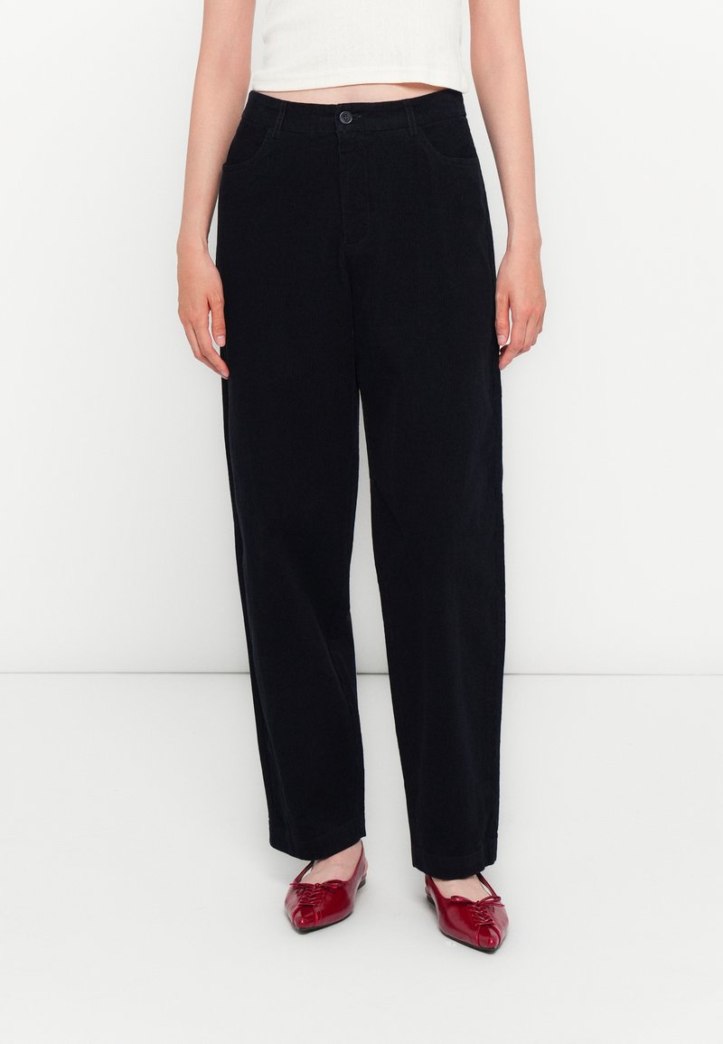 Pantalones de pana amplios de color azul oscuro con cierre de botón y bolsillos frontales, combinados con bailarinas rojas. Textura suave y ajuste relajado.