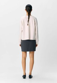 Hellbeige Sweatshirt mit Raglanärmeln, kombiniert mit einem dunkelgrauen, figurbetonten Rock. Glatte Textur, minimalistisches Design, keine sichtbaren Beschläge.