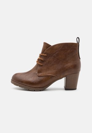 Ruske ankle boot dengan bagian atas kulit bertekstur, tali dekoratif, dan tumit bertumpuk. Memiliki kerah melengkung dan loop kecil di bagian belakang.