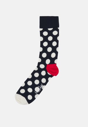 Chaussette marine avec de grands pois blancs, talon rouge et orteil blanc. Fabriquée en tissu doux, avec un logo près de l'orteil.