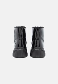 Botas de tornozelo em couro sintético preto com sola ribbed preta e forro suave de pele preta na parte superior. A vista traseira destaca o acabamento brilhante e a textura.