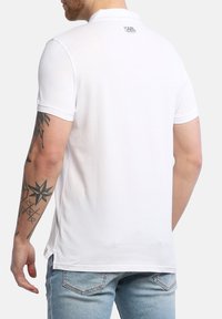 Polo bianco con vestibilità slim, maniche corte e colletto. Presenta un piccolo logo sul retro e spacchi laterali per il comfort.