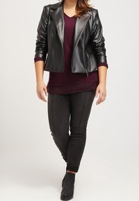 Schwarze Lederbikerjacke mit breiten Revers, getragen über einem burgunderfarbenen Top, kombiniert mit dunklen Jeans und schwarzen Ankle-Boots.