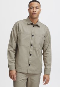 Khaki button-up jacket made from a smooth fabric, featuring two chest pockets, a classic collar, and black buttons for closure.