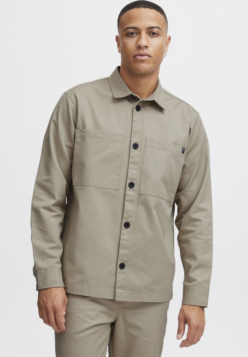 Khaki button-up jacket made from a smooth fabric, featuring two chest pockets, a classic collar, and black buttons for closure.
