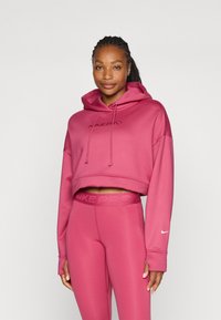 Ružičasti skraćeni dukserica s kapuljačom na vezanje, s natpisom "NIKE PRO" utisnutim na prednjem dijelu, u kombinaciji s odgovarajućim tajicama i akcentima s Nike logom.