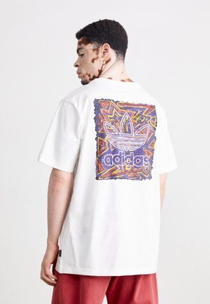 Un t-shirt en coton blanc présente un graphique coloré au dos, affichant le logo Adidas dans une bordure abstraite de formes vibrantes.