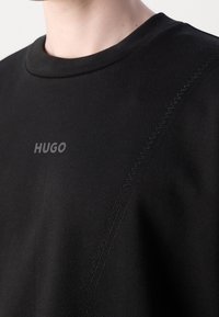 Felpa nera girocollo con logo "HUGO" sul petto e dettaglio diagonale con cuciture sulla spalla destra e sulla manica.