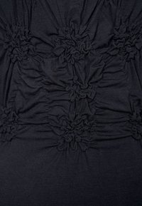 Svart tyg med texturerad rynkning, med samlade sektioner och distinkta blomformade dekorationer som skapar en lagerliknande effekt. Mjukt och elastiskt material.