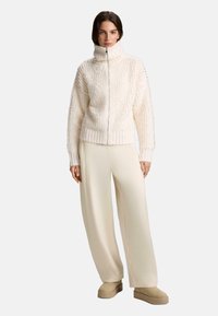 Kréme textúrovaná bunda na zips s vysokým golierom, v páre s svetlo béžovými nohavicami s širokými nohavicami a béžovou obuvou na nazutie. Použité mäkké, teplé materiály.