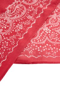 Tissu rouge avec des motifs cachemire et floraux blancs complexes, montrant des coutures détaillées le long des bords.