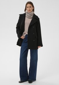 Mustast villasegistust mereväe mantel topelt-rinnaga esiosaga, beežika ribiga kõrgekaelusega kampsun, laia säärega sinised teksapüksid ja mustad pahkluu saapad.