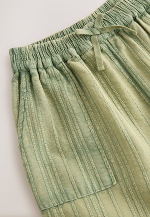 Grønt stof med lodrette striber, elastisk linning og snøre. Indeholder en lomme med lap og har en glat tekstur.