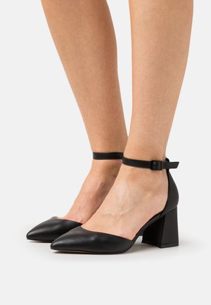 Black leather high-heeled shoes with a pointed toe and ankle strap. Chunky block heel provides stability. Smooth texture and minimalistic design.