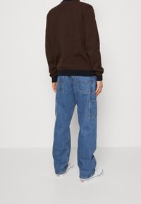 Brun tröja med marinblå ribbade manschetter, kombinerad med lösa blå denim cargo byxor med sidofickor och en klassisk femficksdesign.