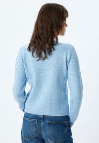 Hellblau gestrickter Pullover mit langen Ärmeln und einem runden Halsausschnitt. Weiche Textur, tailliert, kombiniert mit blauen Jeans.