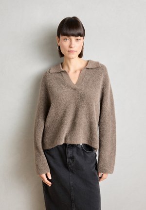Bruine, fuzzy gebreide trui met een V-hals en kraag; gecombineerd met een zwarte denim rok. De textuur lijkt zacht en gezellig.