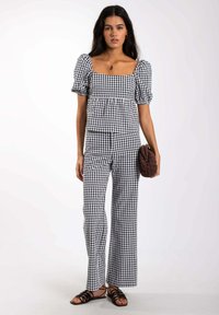 Conjunto de dos piezas en blanco y negro de cuadros vichy que incluye una blusa de escote cuadrado con mangas abullonadas y pantalones acampanados de cintura alta. Tela texturizada.