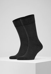 Calcetines de algodón negros con un puño acanalado, diseño simple, longitud hasta el tobillo, textura suave y acabado liso. Posicionados sobre un pedestal blanco.