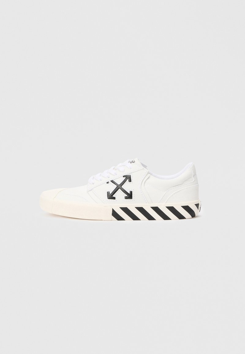White canvas sneaker with black logo and striped black and white sole. Features round toe and lace-up design. Smooth texture.