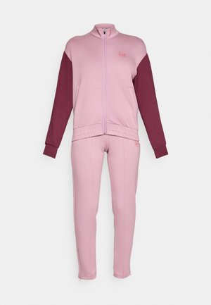 Sett med treningsdress som inkluderer en jakke med glidelås i lys rosa med mørk rosa ermer, kombinert med tettsittende lys rosa bukser, laget av myk tekstil.