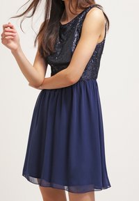 Námořnické modré šaty se zdobeným korzetem a splývavou sukní z chiffonu. Bezrukávový design s kulatým výstřihem a nařaseným pasem.