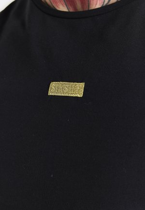 Musta lyhythihainen t-paita, jossa on sileä pinta ja suorakulmainen kultalangalla brodeerattu etiketti rinnassa.