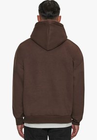 Brauner Kapuzenpullover mit lockerer Passform, gerippten Bündchen und Saum. Der Stoff wirkt weich mit einer glatten Textur. Rückansicht mit minimalen Details.