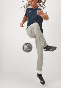Sportlane sinine ja valge särk ning hallid treeningpüksid, kes lööb halli jalgpalli. Mustad spordijalatsid täiustavad riietust.