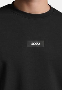 Sort bomuldssweatshirt med rund hals og ribbet tekstur, prydet med et rektangulært hvidt "2XU" logo på brystet.