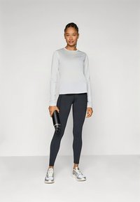 Ljusgrå långärmad topp, svarta leggings och gråa sneakers. Personen håller en svart vattenflaska med slät yta och modern design.