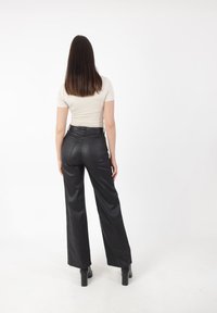 Pantalones de cuero negro de pierna ancha con una textura suave, cintura alta y bolsillos, combinados con una blusa ajustada de manga corta color beige.