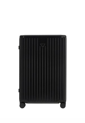 Valise rigide noire avec des rainures verticales, quatre roues et un petit logo Guess au centre sur fond blanc.