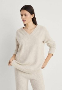 Lichtbeige gebreide trui met een V-hals, geribde manchetten en zoom. Zacht, gestructureerd materiaal; gecombineerd met bijpassende lichtbeige broek.