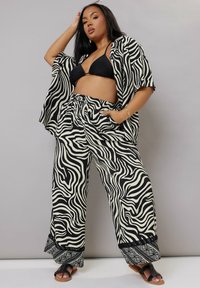 Svart och krämfärgad zebra-mönstrad outfit bestående av en lös skjorta och vida byxor med dekorativ fåll och elastisk midja.
