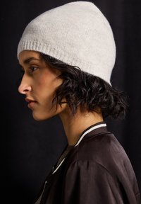 Berretto in maglia grigio chiaro con una consistenza morbida; parte superiore arrotondata e bordo a coste. Accompagnato da una giacca bomber scura con accenti bianchi.