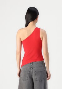 Rode top met één schouder, gemaakt van rekbaar materiaal; naadloos ontwerp met een asymmetrische onderkant. Gecombineerd met hoge grijze denim shorts.