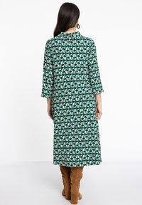 Langes grünes Kleid mit einem grafischen Muster aus Ovalen in Teal, Braun und Creme, mit einer durchgeknöpften Rückseite und drei Viertelärmeln.