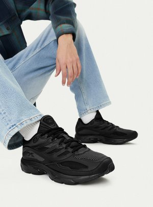 Person trägt hellblaue Jeans, weiße Socken und schwarze Sportschuhe und sitzt mit einem erhobenen Knie.