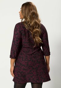 Schwarzes Kleid mit einem weinroten Blumenmuster, drei Viertel-Ärmeln und einem schwingenden Rock. Glatte Textur mit dezenten Details.