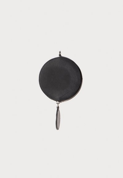 Porte-monnaie rond en cuir noir avec fermeture éclair, présentant une texture lisse et une étiquette suspendue. Design minimaliste, sans motifs ni accents.